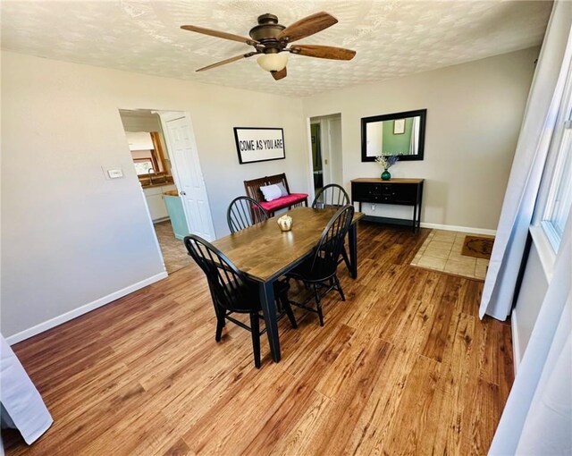 dining room featuring ceiling fan, baseboards, a textured ceiling, and light wood-style flooring