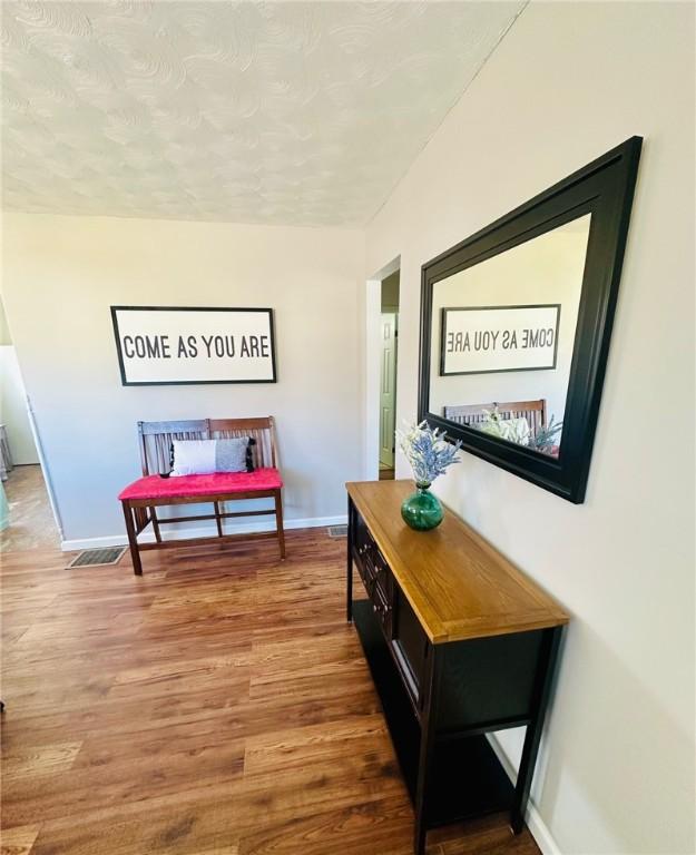 hallway with baseboards, visible vents, wood finished floors, and a textured ceiling