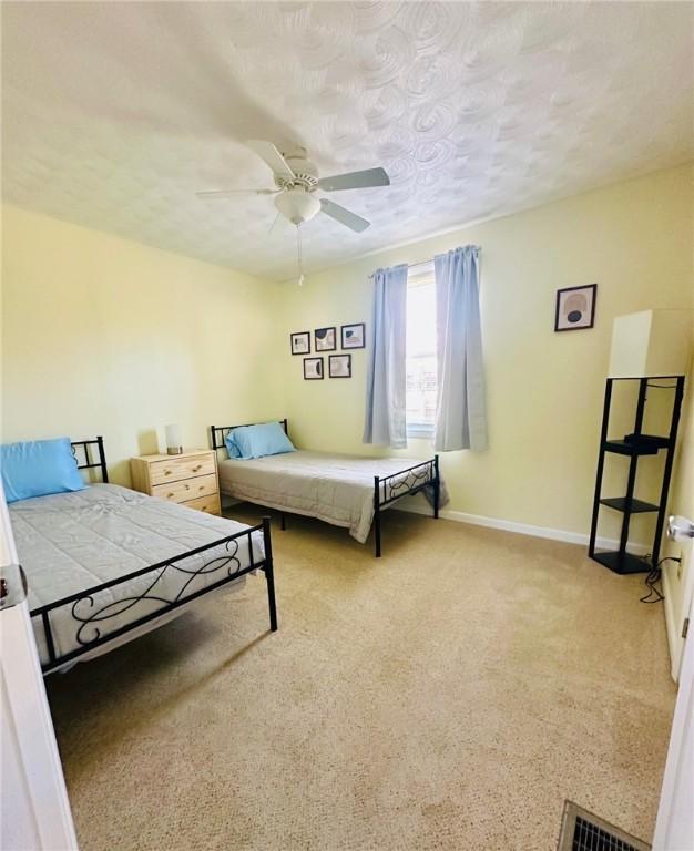 bedroom featuring baseboards, visible vents, light colored carpet, and ceiling fan