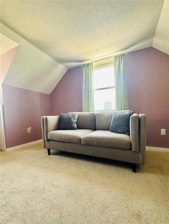 interior space with vaulted ceiling, baseboards, a textured ceiling, and light colored carpet