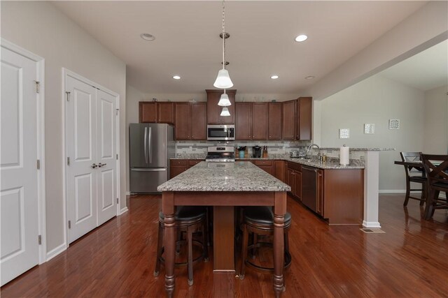 kitchen with stainless steel appliances, a sink, dark wood-style flooring, baseboards, and a breakfast bar