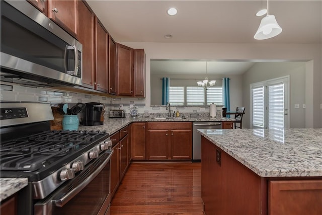 kitchen featuring dark wood finished floors, stainless steel appliances, an inviting chandelier, a sink, and decorative light fixtures