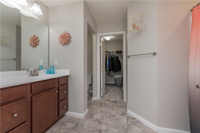 full bath with baseboards, vanity, a spacious closet, and toilet