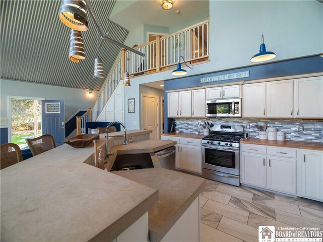 kitchen featuring decorative backsplash, a high ceiling, appliances with stainless steel finishes, and a sink