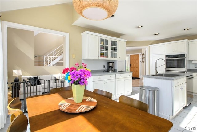kitchen with stainless steel appliances, a kitchen island with sink, white cabinetry, and glass insert cabinets