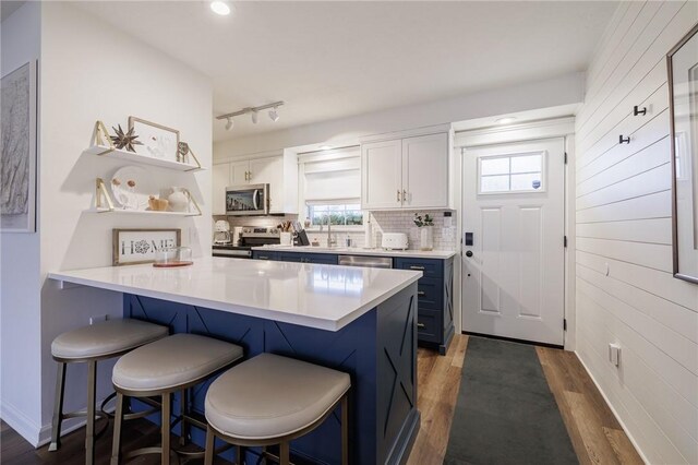 kitchen with wood finished floors, a breakfast bar area, stainless steel appliances, white cabinets, and a peninsula