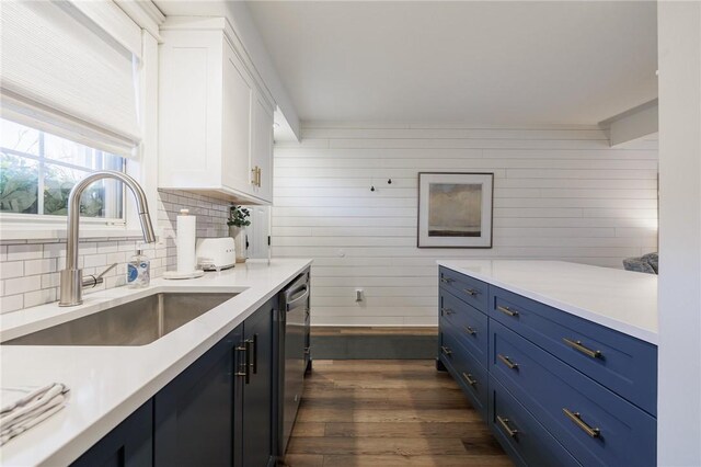 kitchen featuring dark wood-style flooring, white cabinetry, wood walls, and a sink