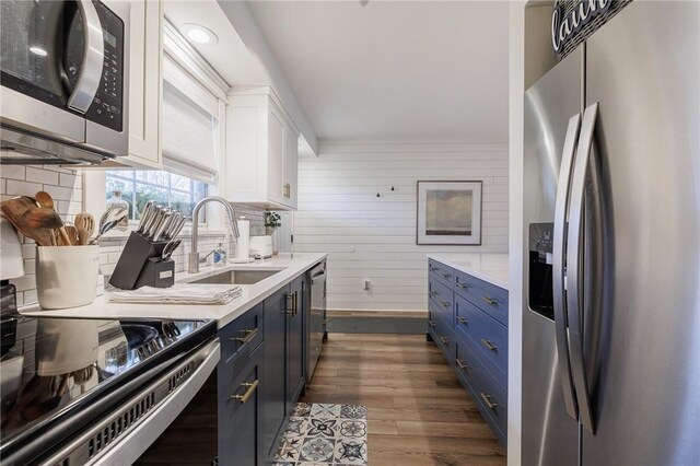 kitchen featuring blue cabinets, a sink, dark wood finished floors, light countertops, and appliances with stainless steel finishes