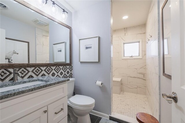 bathroom with a tile shower, toilet, vanity, and visible vents