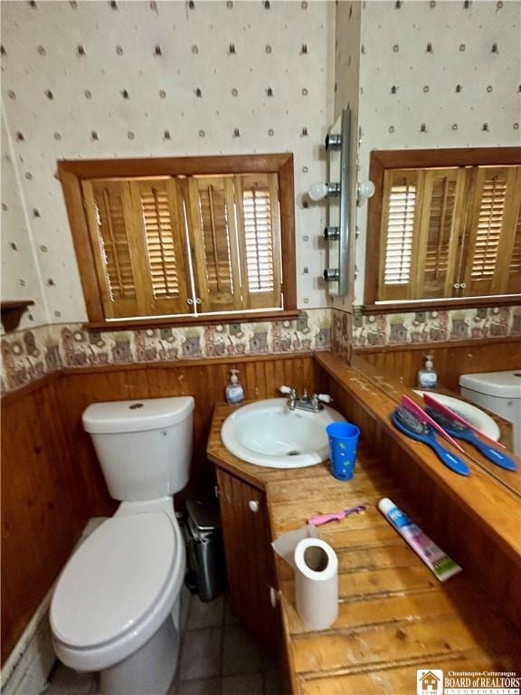bathroom with wallpapered walls, a wainscoted wall, vanity, and toilet