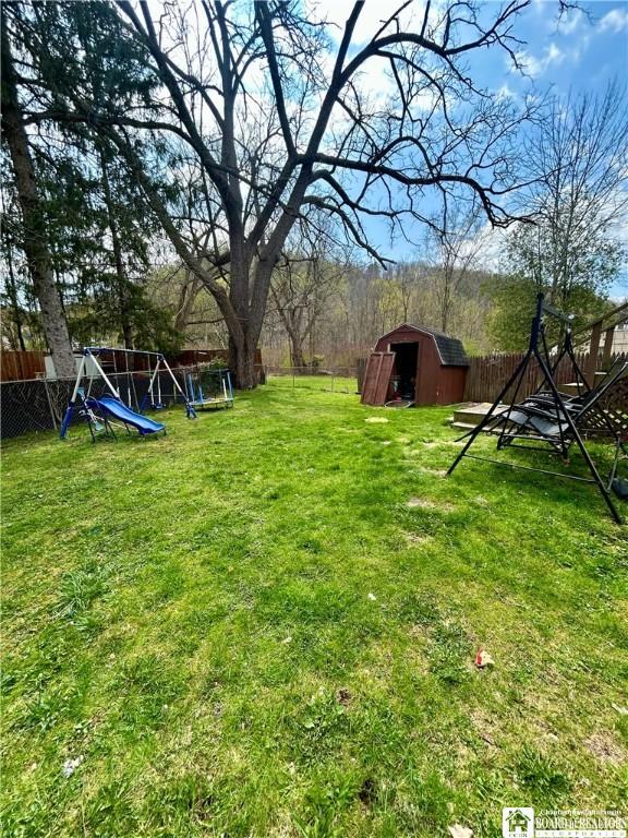 view of yard featuring an outdoor structure, a storage unit, a fenced backyard, and a playground