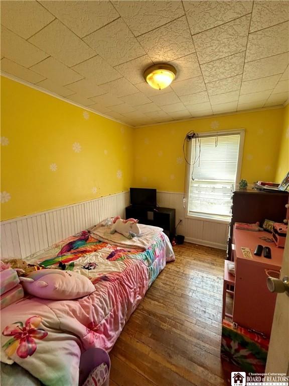 bedroom featuring wood-type flooring, a wainscoted wall, and ornamental molding