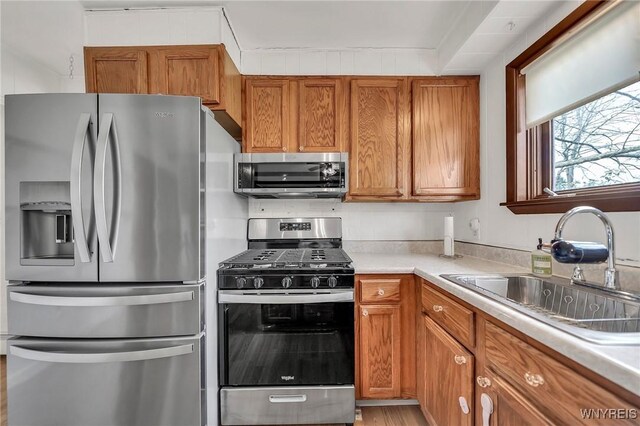 kitchen with light countertops, a sink, light wood-type flooring, brown cabinetry, and appliances with stainless steel finishes