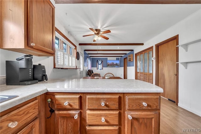 kitchen with a peninsula, light wood-type flooring, ceiling fan, brown cabinetry, and light countertops