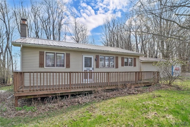 rear view of house featuring a yard, a chimney, metal roof, and a deck