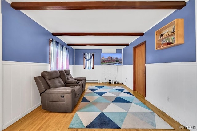 living area featuring beamed ceiling, wainscoting, wood finished floors, and a baseboard heating unit