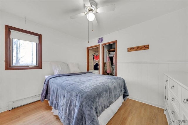 bedroom featuring a baseboard heating unit, ceiling fan, wainscoting, and light wood-type flooring