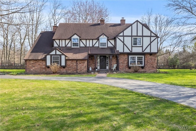 english style home with a chimney, brick siding, stucco siding, and a front yard