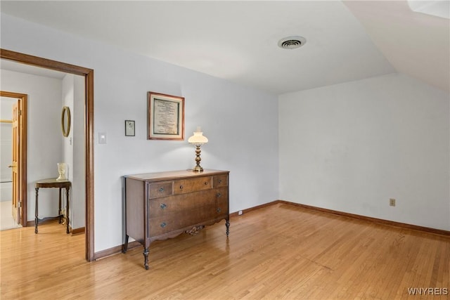 interior space featuring vaulted ceiling, light wood-style flooring, visible vents, and baseboards