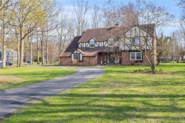 tudor house featuring a chimney, aphalt driveway, a front yard, and brick siding