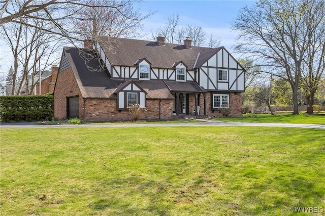 english style home with brick siding, a front lawn, a chimney, and a garage