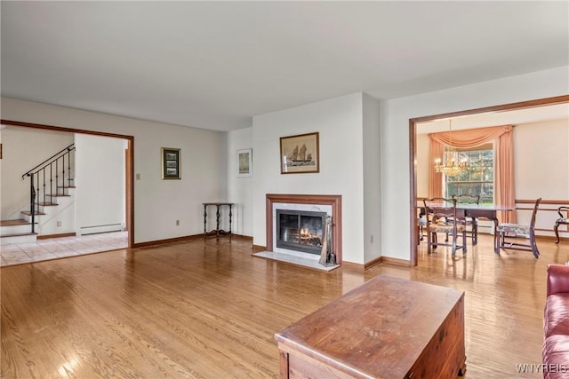 living area with light wood finished floors, a fireplace with flush hearth, an inviting chandelier, stairway, and a baseboard radiator