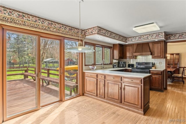kitchen with stainless steel electric stove, a peninsula, custom exhaust hood, light wood-style floors, and light countertops