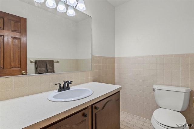 bathroom with wainscoting, toilet, vanity, and tile walls