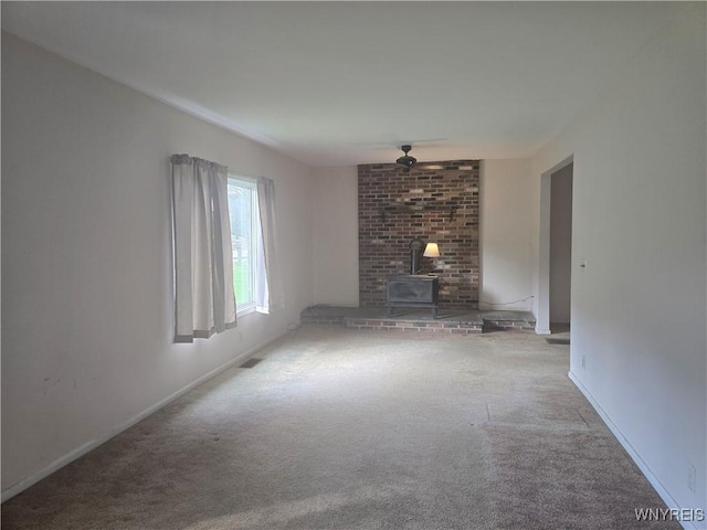 unfurnished living room featuring ceiling fan, carpet floors, a wood stove, baseboards, and visible vents