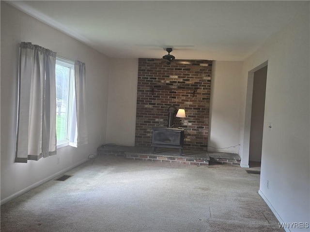 unfurnished living room featuring carpet flooring, a wood stove, a ceiling fan, and visible vents