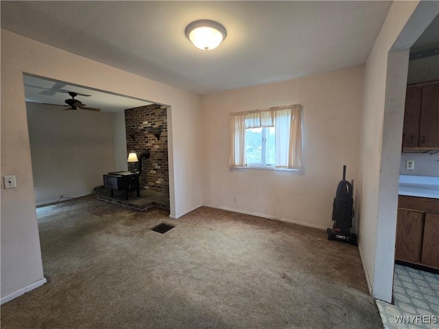 unfurnished living room featuring ceiling fan, a wood stove, carpet, baseboards, and visible vents
