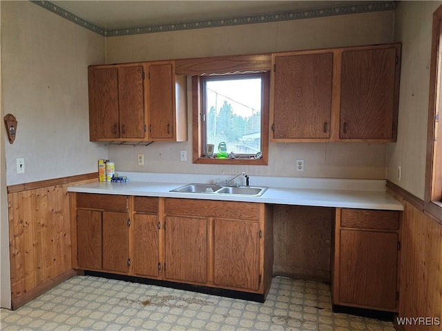 kitchen featuring wainscoting, light floors, a sink, and brown cabinets