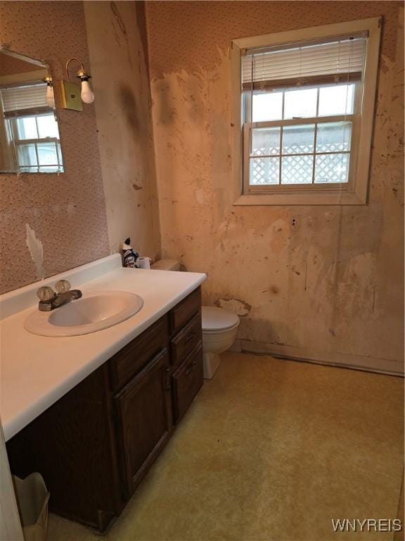bathroom with wallpapered walls, toilet, vanity, and a healthy amount of sunlight