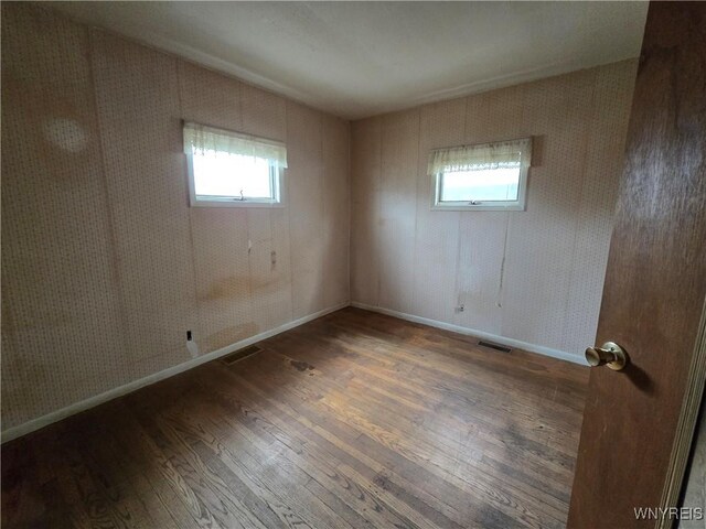empty room featuring wood finished floors, visible vents, and baseboards