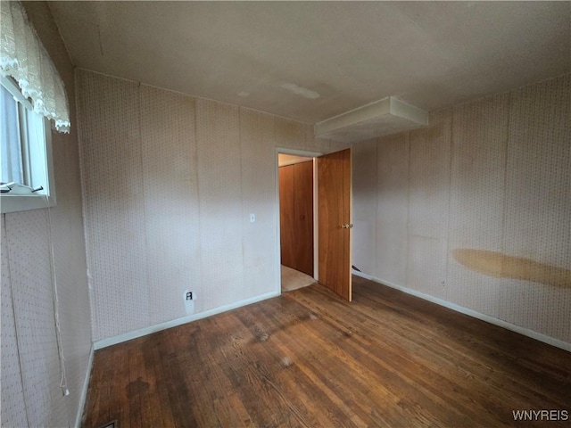 empty room featuring wallpapered walls, wood finished floors, and baseboards