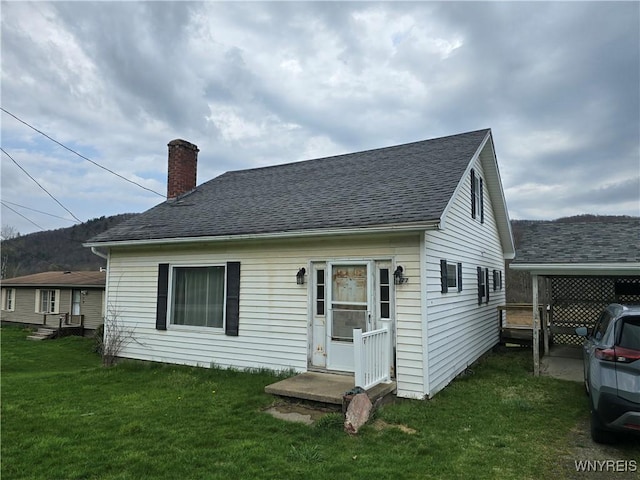 rear view of house featuring entry steps, a lawn, a shingled roof, and a chimney