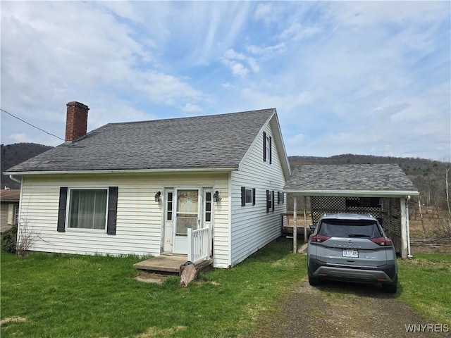 view of front facade with a front lawn, a carport, driveway, a chimney, and a shingled roof