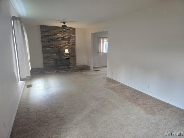 unfurnished living room with baseboards, visible vents, carpet, ceiling fan, and a wood stove