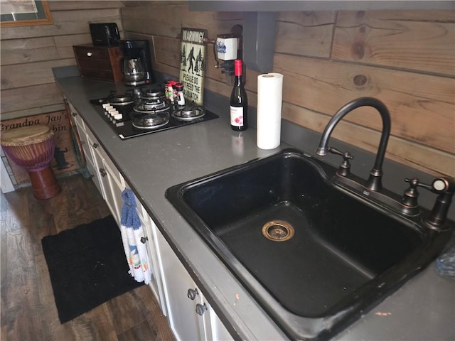 interior details with a sink, white cabinetry, black gas stovetop, wooden walls, and dark wood-type flooring