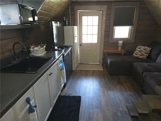 kitchen with white cabinets, dark wood finished floors, lofted ceiling, wooden walls, and a sink