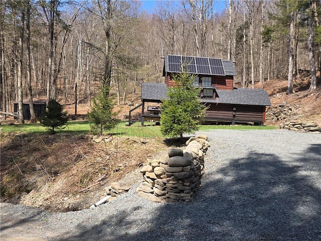 view of front of house featuring solar panels, a wooded view, and a shingled roof
