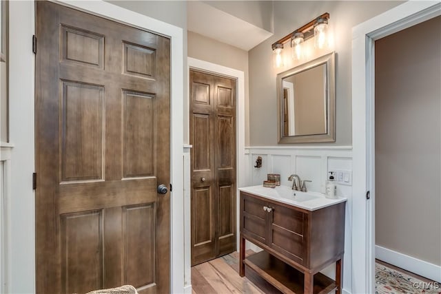 5410 N Shore Rd, Greig, NY 13312 - bathroom featuring vanity, a decorative wall, a wainscoted wall, and wood finished floors