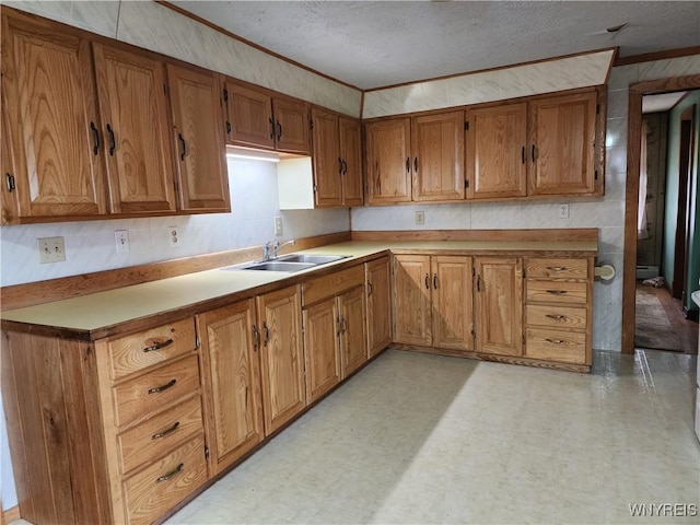 kitchen featuring brown cabinetry, light floors, ornamental molding, and a sink