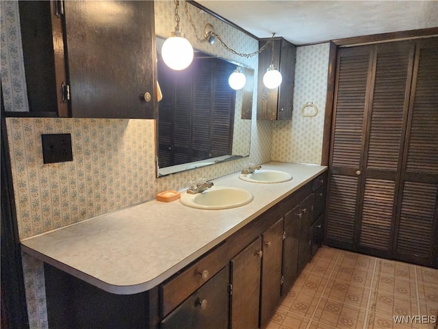 bathroom with a sink, wallpapered walls, and double vanity