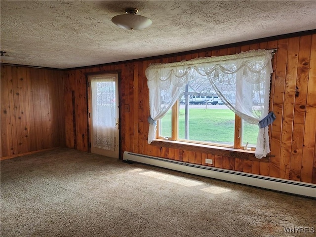 unfurnished room with baseboard heating, wood walls, carpet, and a textured ceiling