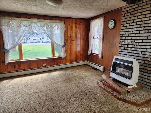 unfurnished living room with carpet flooring, a textured ceiling, heating unit, wooden walls, and a wood stove