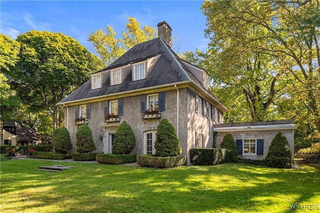view of front of home featuring stucco siding, a chimney, and a front yard
