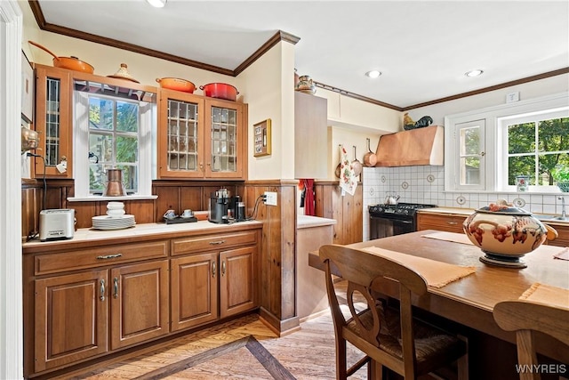 kitchen with ornamental molding, black gas stove, a healthy amount of sunlight, and custom range hood
