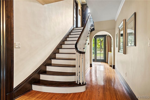 staircase featuring baseboards, wood finished floors, arched walkways, and ornamental molding