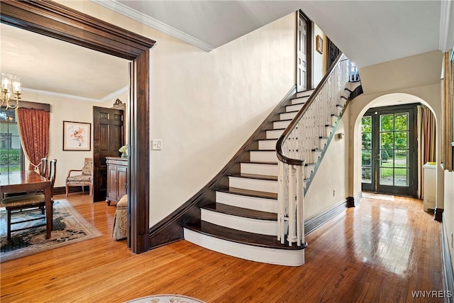staircase featuring an inviting chandelier, ornamental molding, arched walkways, baseboards, and hardwood / wood-style flooring